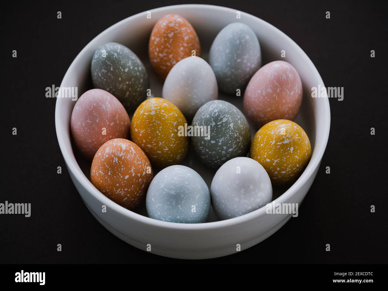 Blick von oben auf bunte Ostereier in Schale auf schwarz Hintergrund Stockfoto