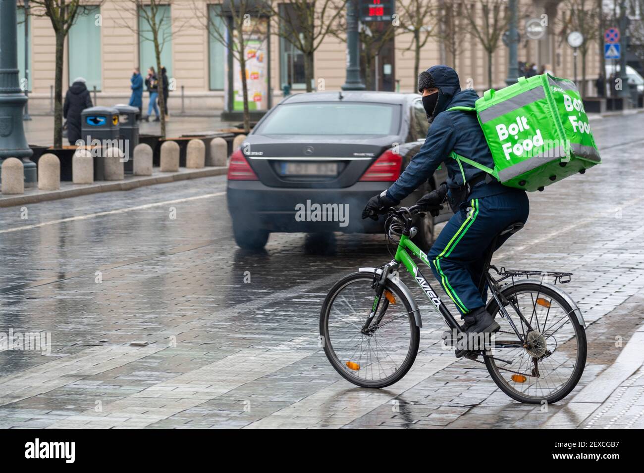 Fahrer mit Fahrrad und Maske unter dem Regen arbeitet für Bolt Food, Online-Food-Bestellung und Lieferservice, die Bestellungen über eine mobile App nimmt Stockfoto