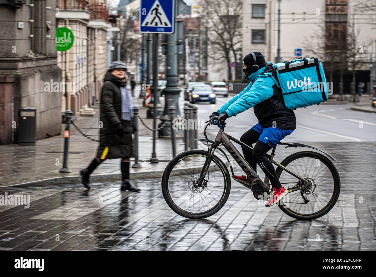 Fahrer mit Fahrrad und Maske unter dem Regen arbeitet für Wolt, Online-Food-Bestellung und Lieferservice, die Bestellungen über eine mobile App nimmt Stockfoto