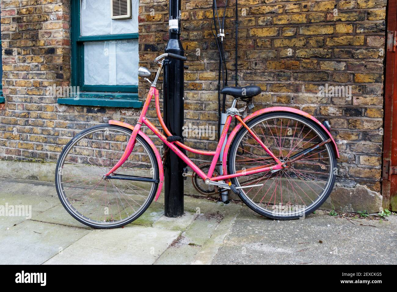 Ein altmodisches, pinkfarbenes Fahrrad, das an einen Lampenpfosten in Islington, London, Großbritannien, gekettet ist Stockfoto