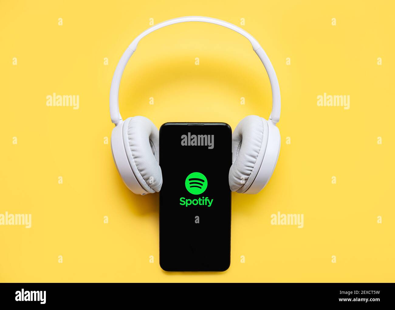 Spotify-Anwendungssymbol auf schwarzem Bildschirm des Smartphones mit weißem Display Kabelloser Kopfhörer auf gelbem Hintergrund Stockfoto