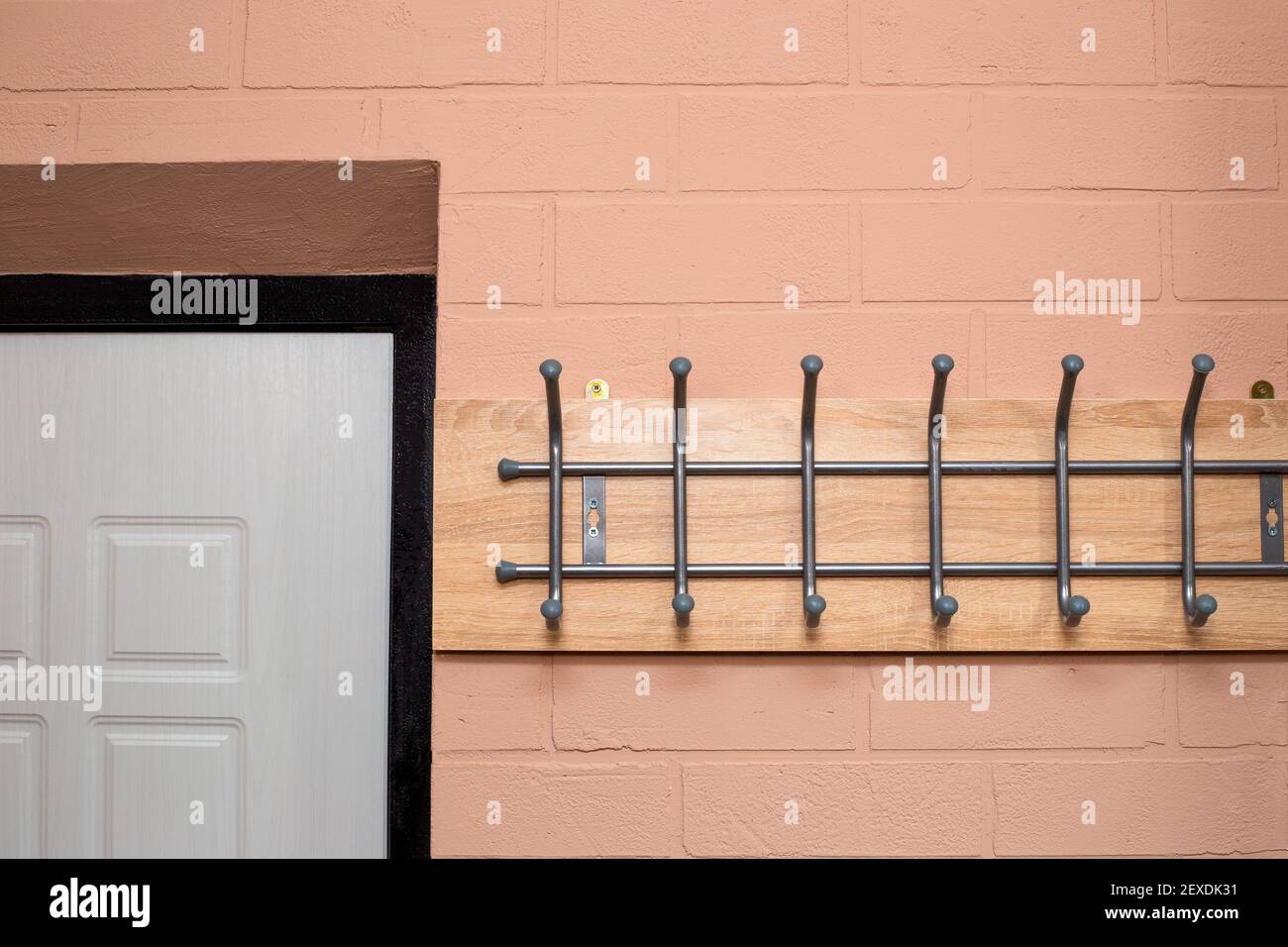 Flur in der Wohnung. Die Wände sind mit Kitt mit einem Mauerwerk-Effekt dekoriert. Weiße Vordertür und hölzerne Wandhalterung mit Haken. Stockfoto