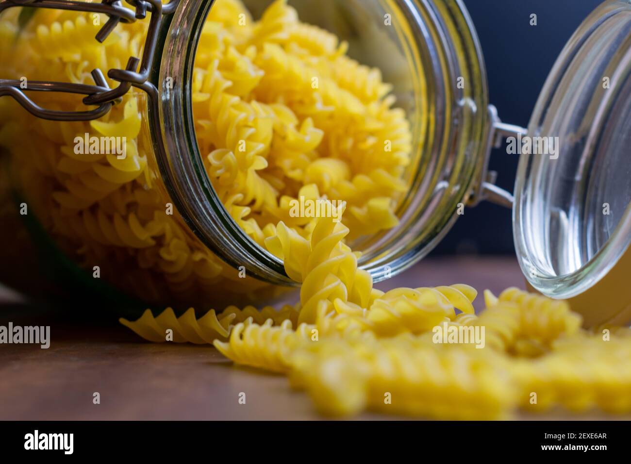 Fussili Pasta aus einem großen luftdichten Glas fallen. Rohe trockene Nudeln in Null-Abfall-Glasbehälter. Chaotisch Lebensmittelkomposition auf dunklem Hintergrund mit Stockfoto