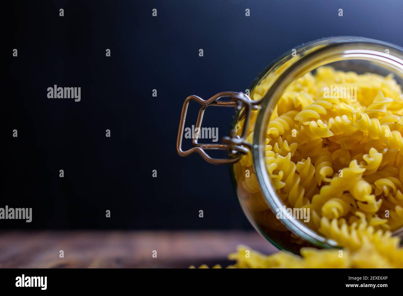 Fussili Pasta aus einem großen luftdichten Glas fallen. Rohe trockene Nudeln in Null-Abfall-Glasbehälter. Chaotisch Lebensmittelkomposition auf dunklem Hintergrund mit Stockfoto