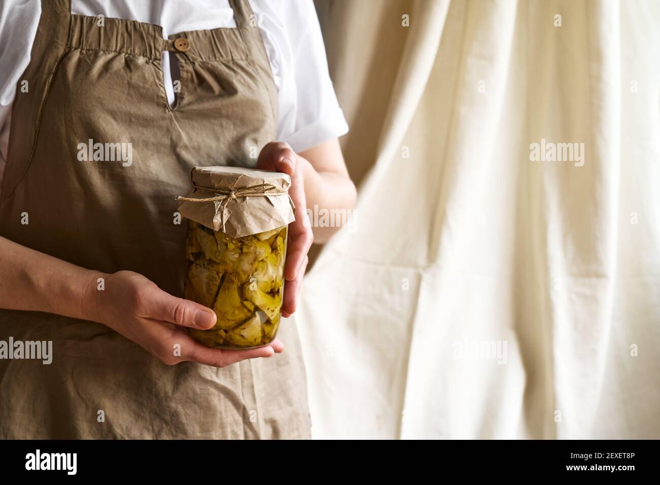 Frau hält ein Glas mit Artischocken aus der Dose in Öl. Artischocken im Glas mit Olivenöl und Kräutern. Hausgemachte gesunde Ernährung Stockfoto