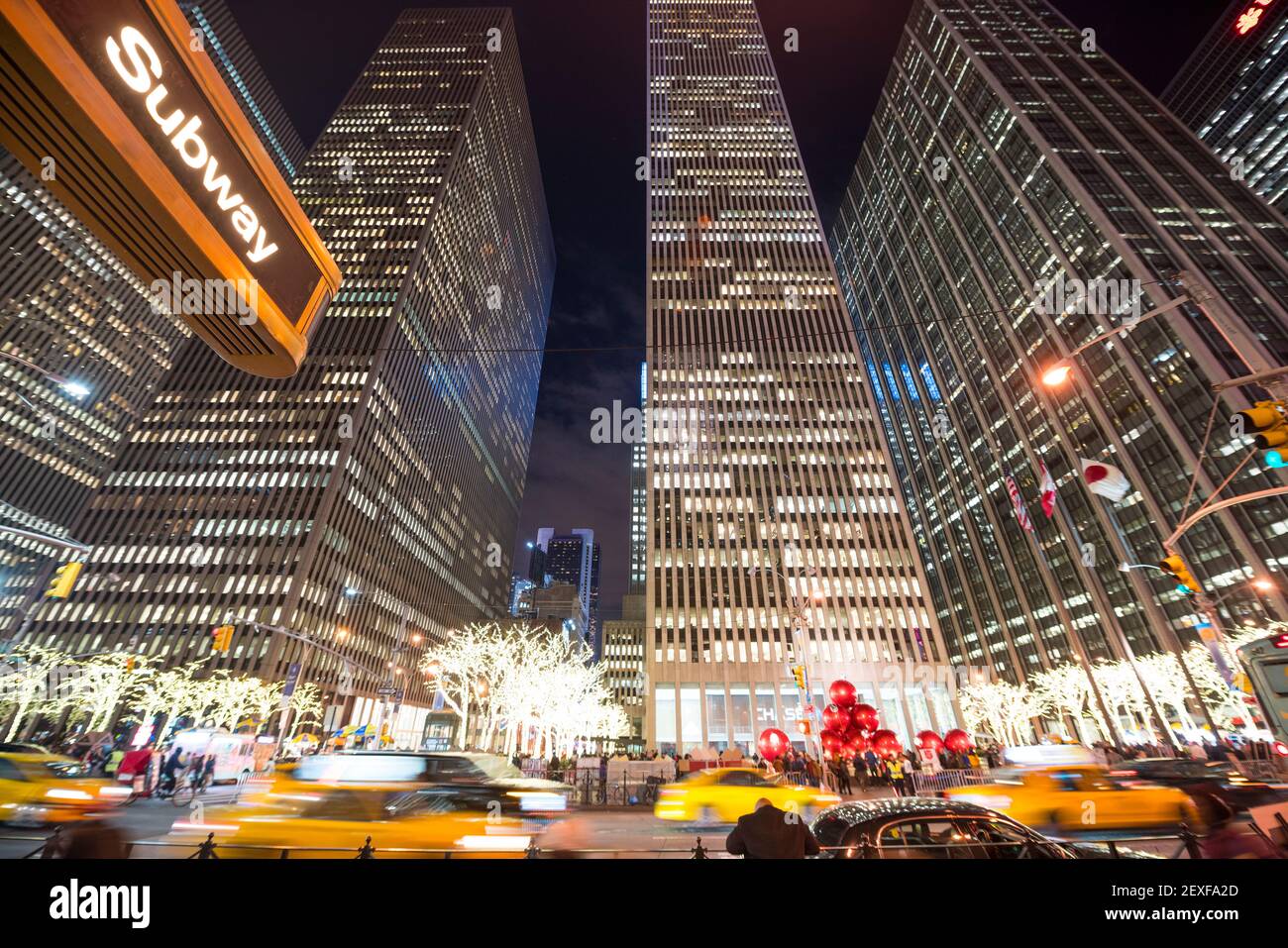 Midtown Sixth Avenue während der Weihnachtsfeiertage in der Nacht in New York City NY wird in den Reihen der Hochhäuser Verkehr durchfahren. Stockfoto