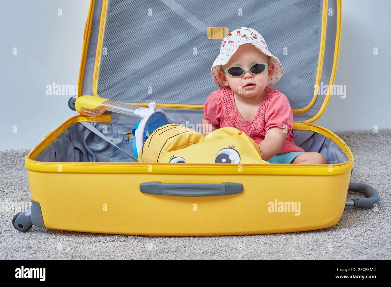 Reisekonzept. Das Kind sitzt in einem Koffer mit sommerlichen Dingen für einen Urlaub am Meer. Stockfoto