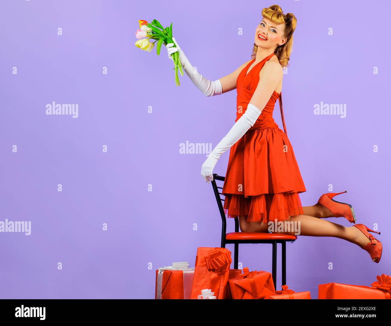 Valentinstag. Glückliches Mädchen mit Geschenk und Strauß von Tulpen. Lächelnde Frau im roten Kleid mit Blumen und Geschenk Stockfoto
