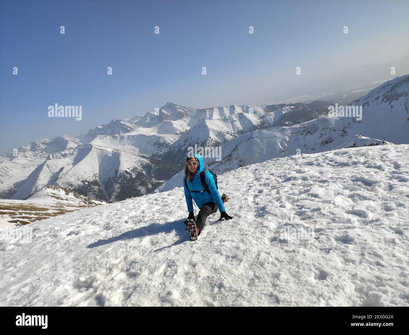 Eine Touristin in einer blauen Jacke macht Splits auf dem Gipfel des Berges. Stockfoto
