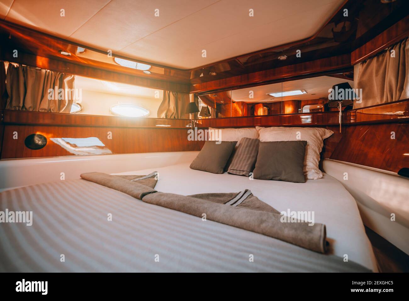 Ein Weitwinkel-Fragment eines Innenraums einer luxuriösen Bootshütte mit einem großen ordentlich gemachten Bett, lackierter Holzvertäfelung Dekoration, Streifen von Spiegeln und ein Stockfoto