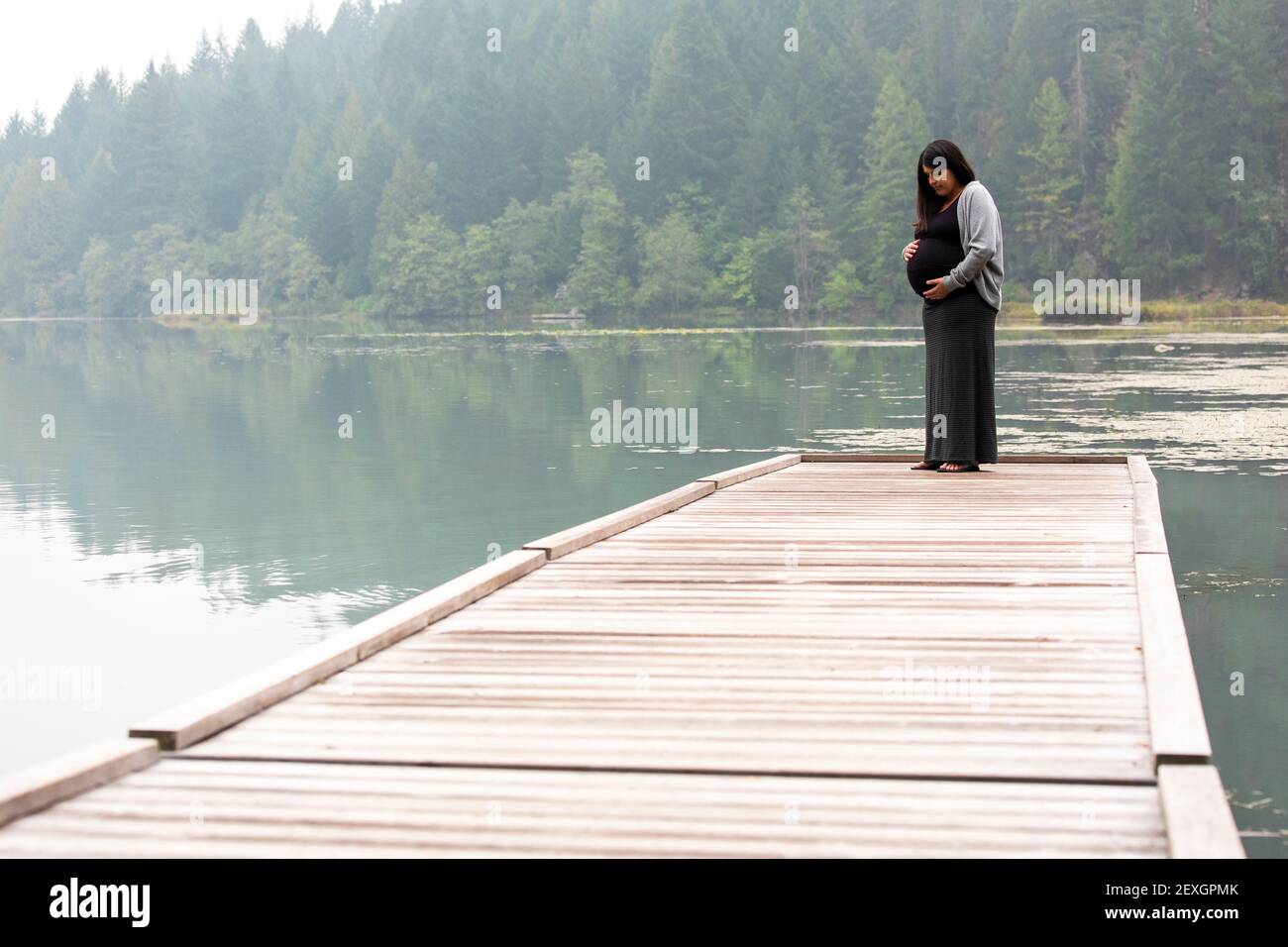 Unverkennbare schwangere Frau auf dem Dock stehend und auf ihren Bauch schauend Stockfoto