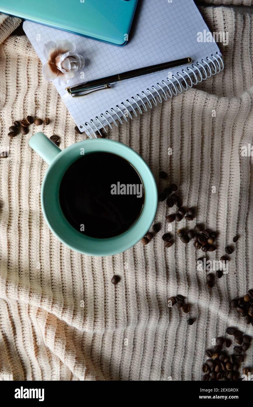 tasse Kaffee neben Notebook mit Handy und Stift darauf Stockfoto