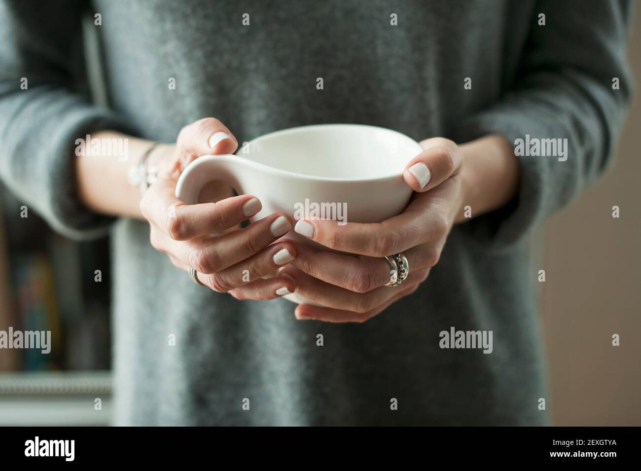 Nahaufnahme einer Frau in warmer Strickmode, Hände mit einem weißen Becher. Entspannte, gemütliche Atmosphäre, Home Lounging Lifestyle-Konzept Stockfoto