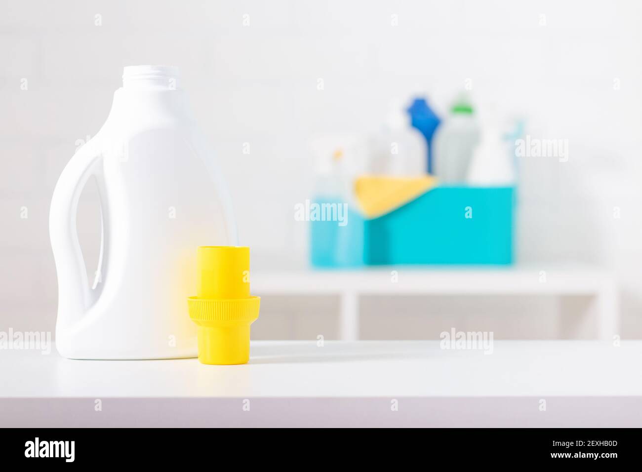 Weiße Chlor-Flasche mit gelbem Deckel Mock-up. Giftiges Reinigungsmittel. Reinigungszubehör im Hintergrund. Verwendung des Messbechers. Stockfoto