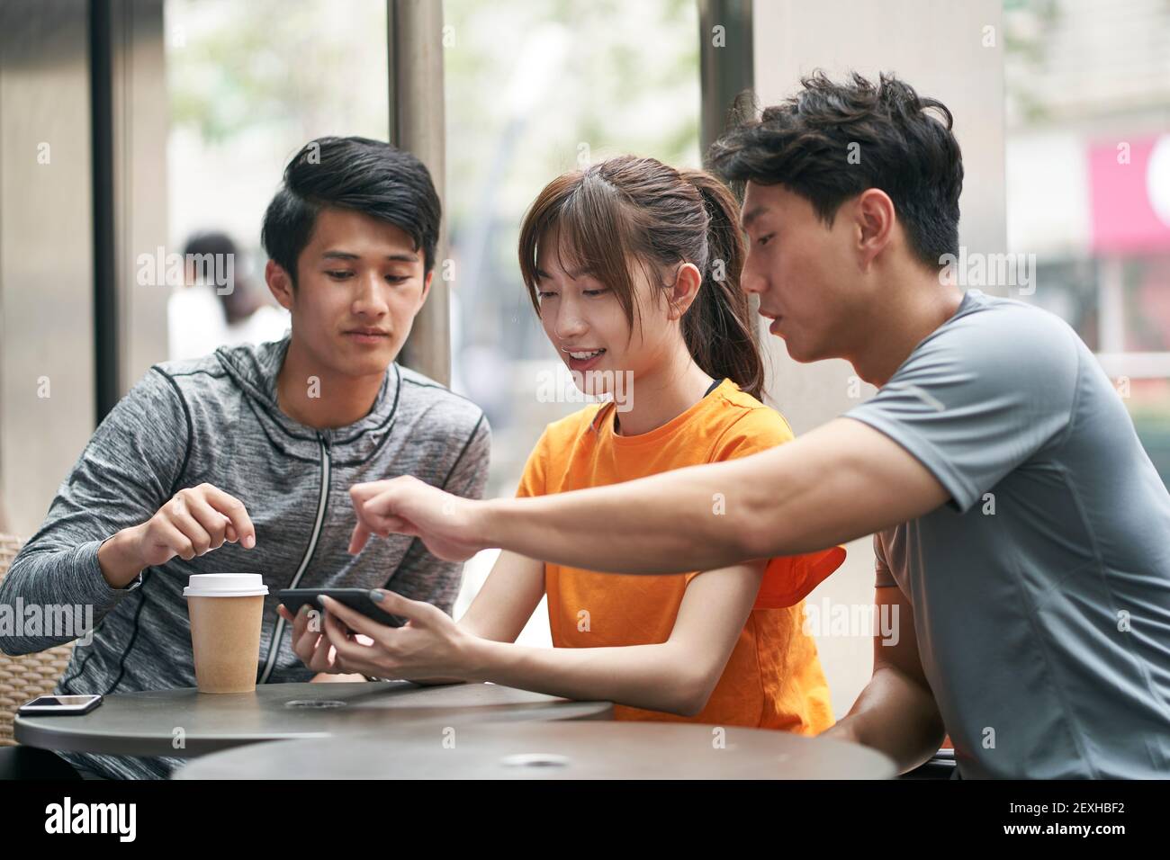 Drei junge asiatische Erwachsene, die im Café im Freien sitzen Handy zusammen Stockfoto