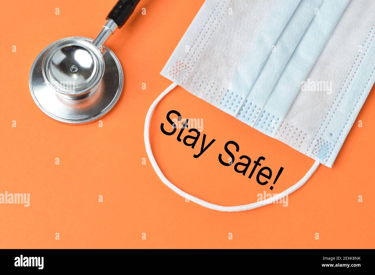 Stethoskop und Gesichtsmaske über orangefarbenem Hintergrund mit STAY SAFE geschrieben!. Stockfoto