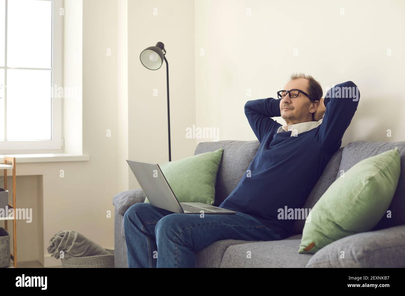 Mann machte eine Pause von der Arbeit, saß auf einem Sofa mit einem Laptop und legte seine Hände hinter seinen Kopf. Stockfoto
