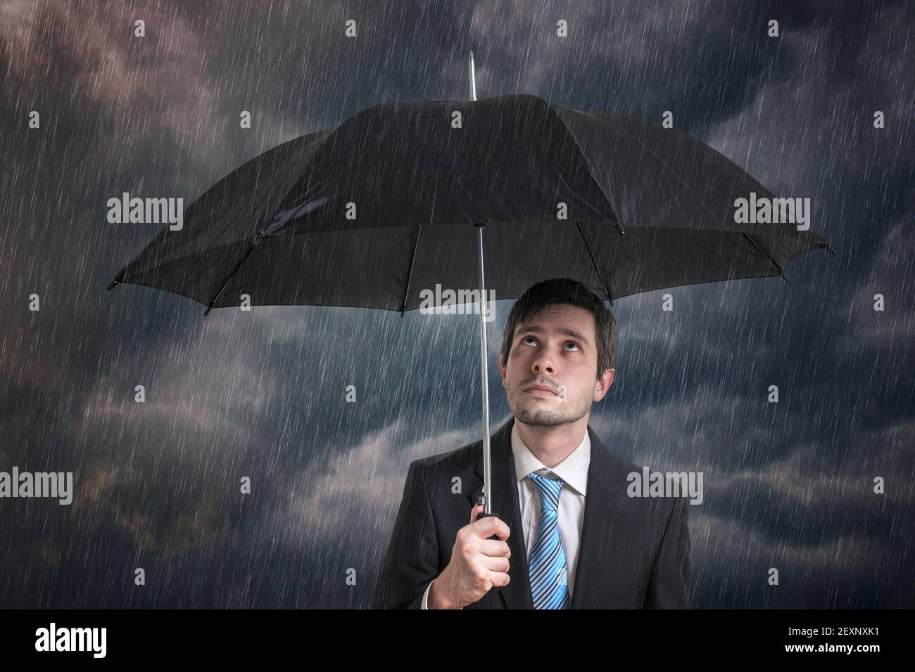 Pessimistischer Geschäftsmann mit schwarzem Regenschirm im Sturm. Stockfoto