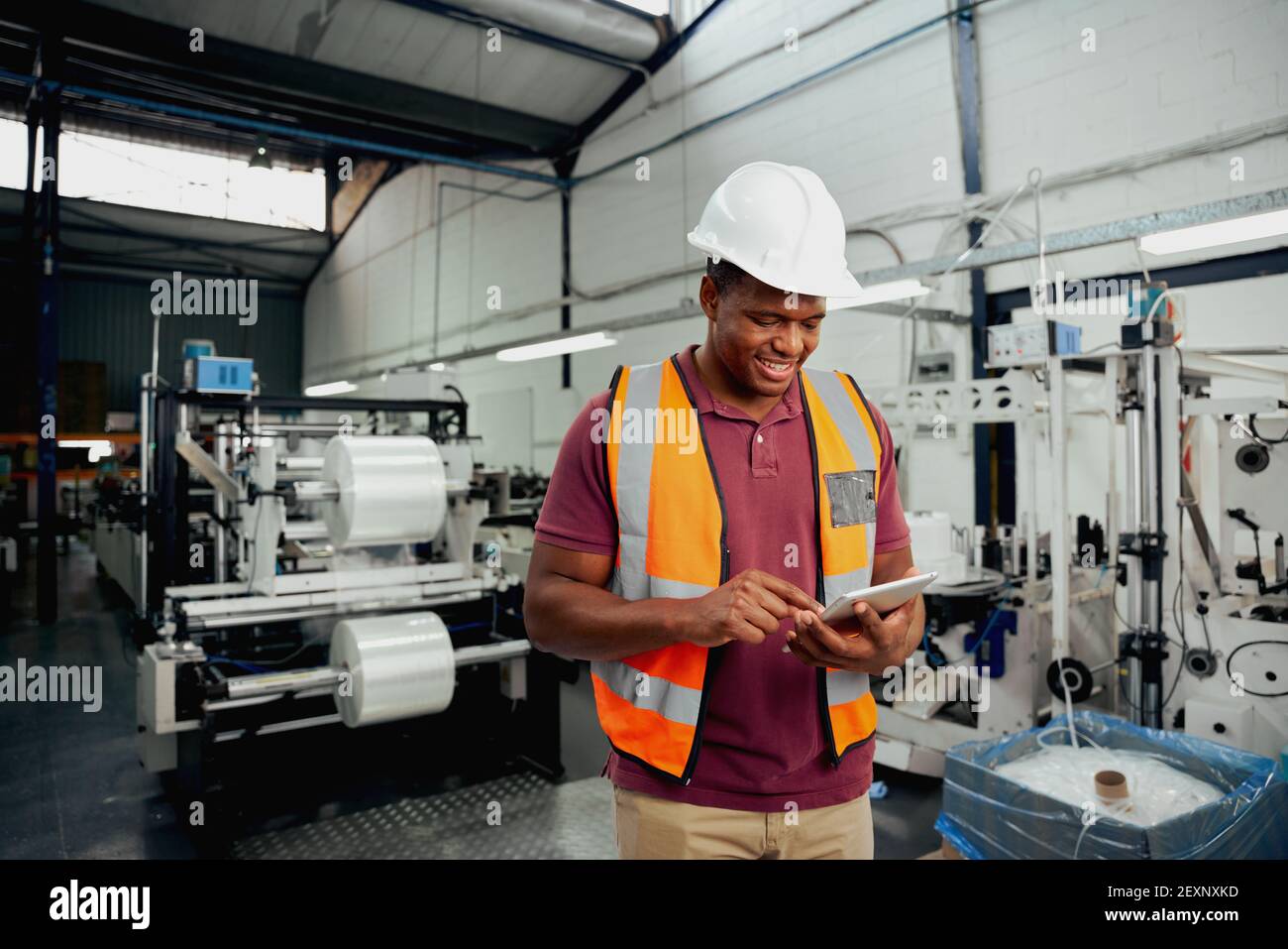Lächelnder junger afrikanischer männlicher Mitarbeiter mit digitalem Tablet während der Arbeit In der Industrie Stockfoto