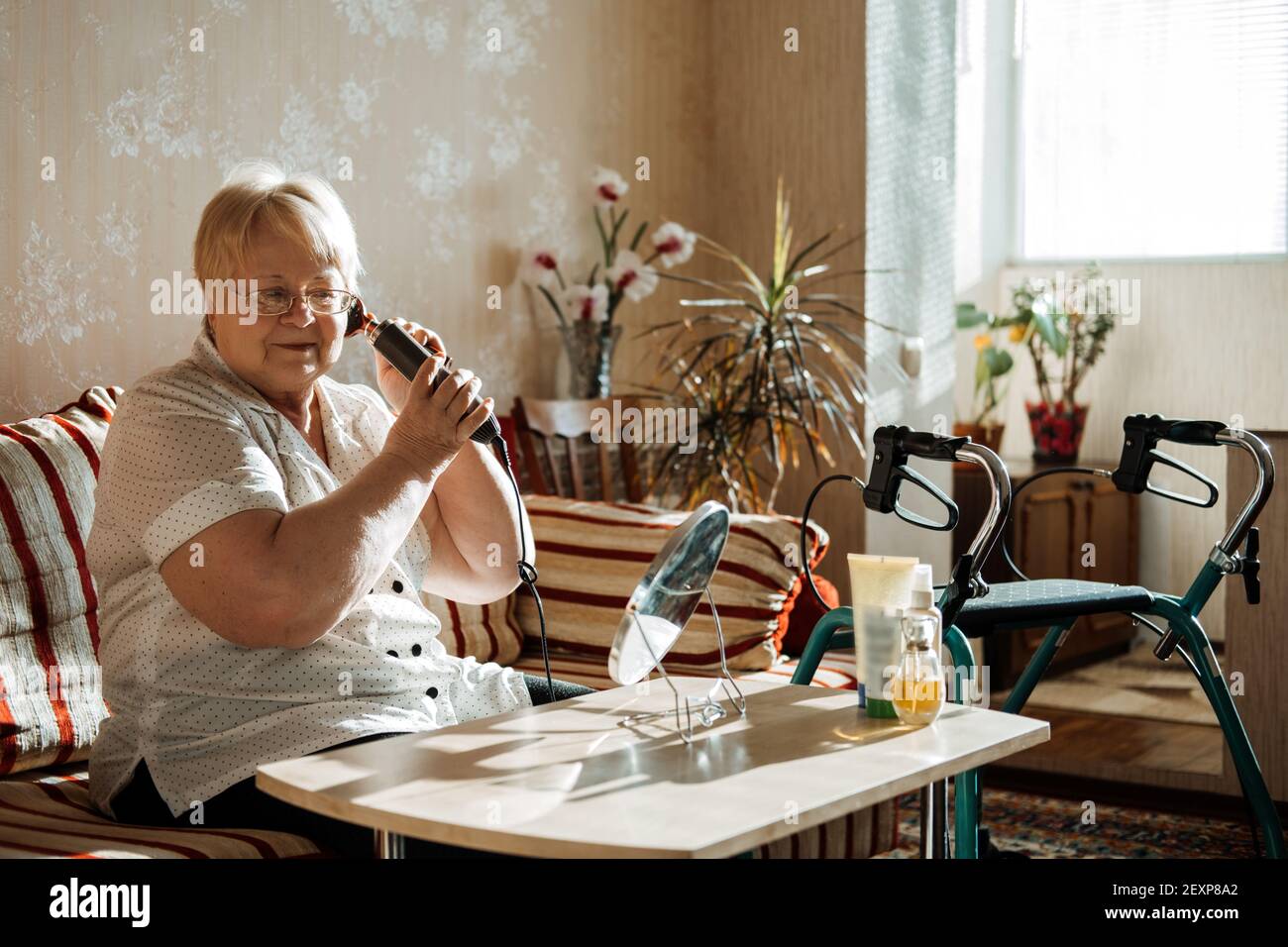 Ältere Schönheit und Hautpflege. Ältere ältere Menschen plus Größe blonde Frau mit Behinderung Styling Haar in der Nähe des Spiegels zu Hause. Stockfoto