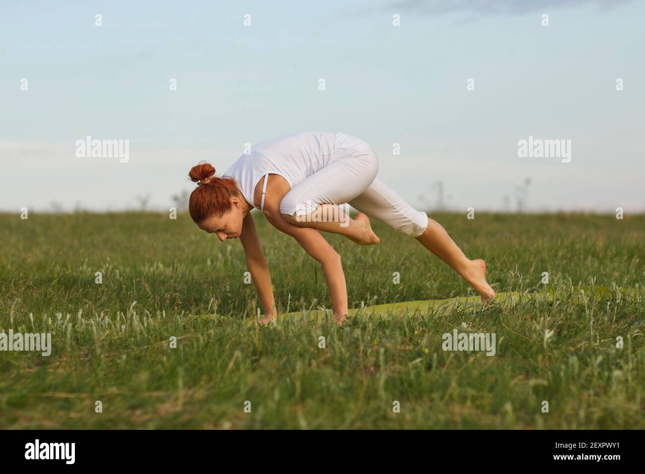 Junge Frau tut Balancing-Übung beim Üben Yoga auf grün Sommerwiese Stockfoto