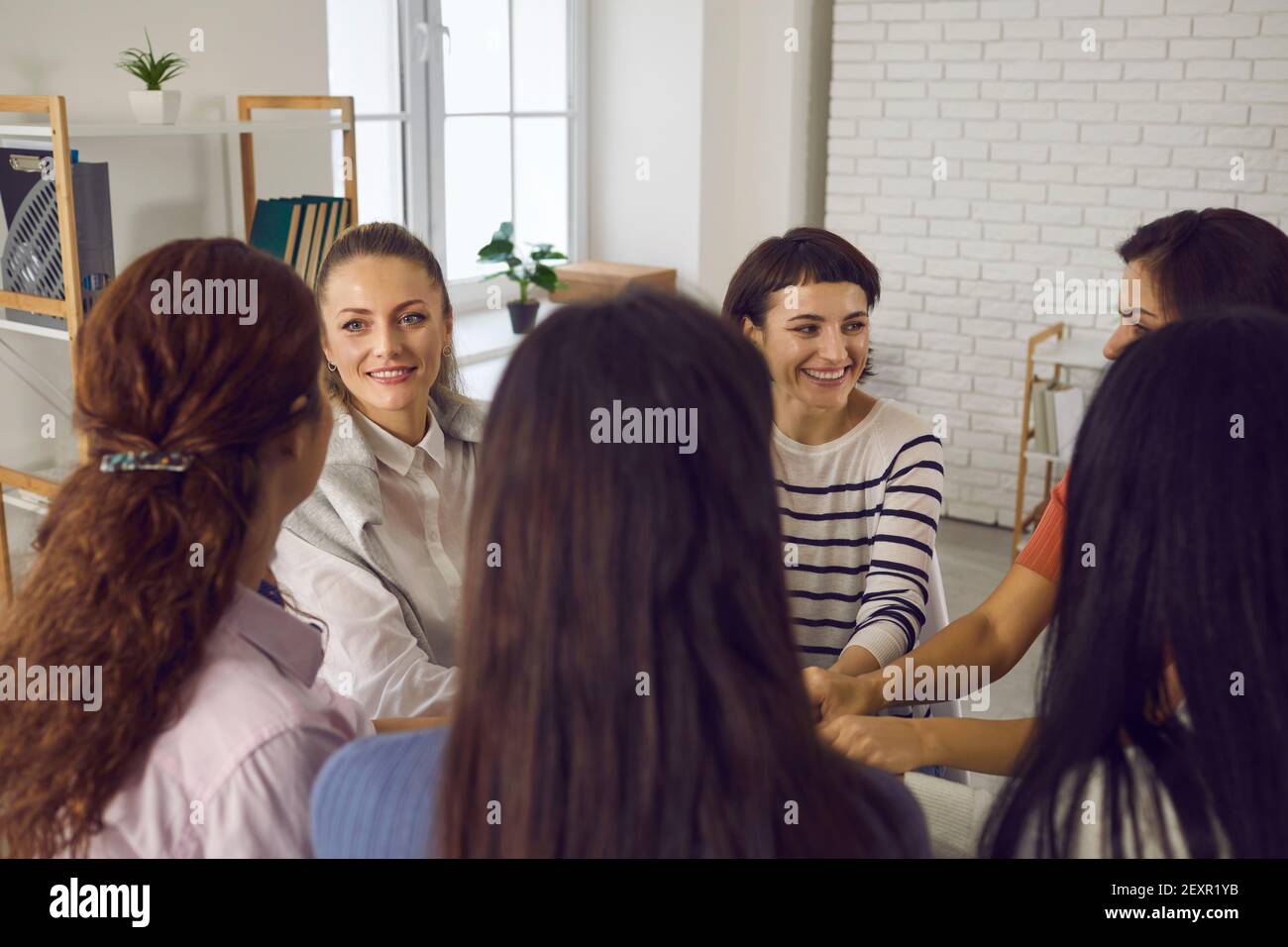 Glückliche Frauen sitzen im Kreis und halten Hände in Unternehmen Meeting- oder Gruppentherapiesitzung Stockfoto