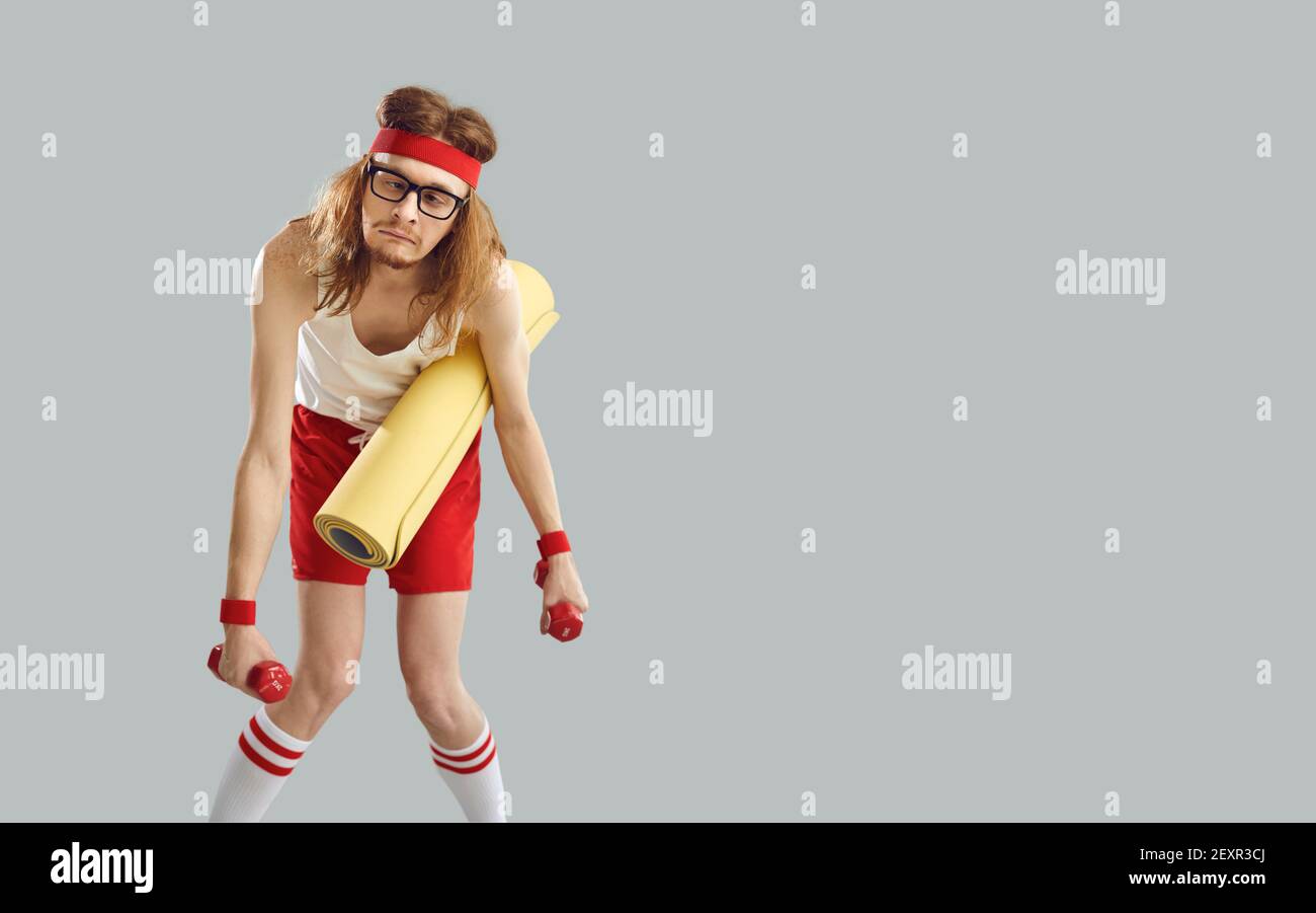 Lustige erschöpft mager Mann hält Turnhalle Matte und Hanteln stehen Vor grauem Hintergrund Stockfoto