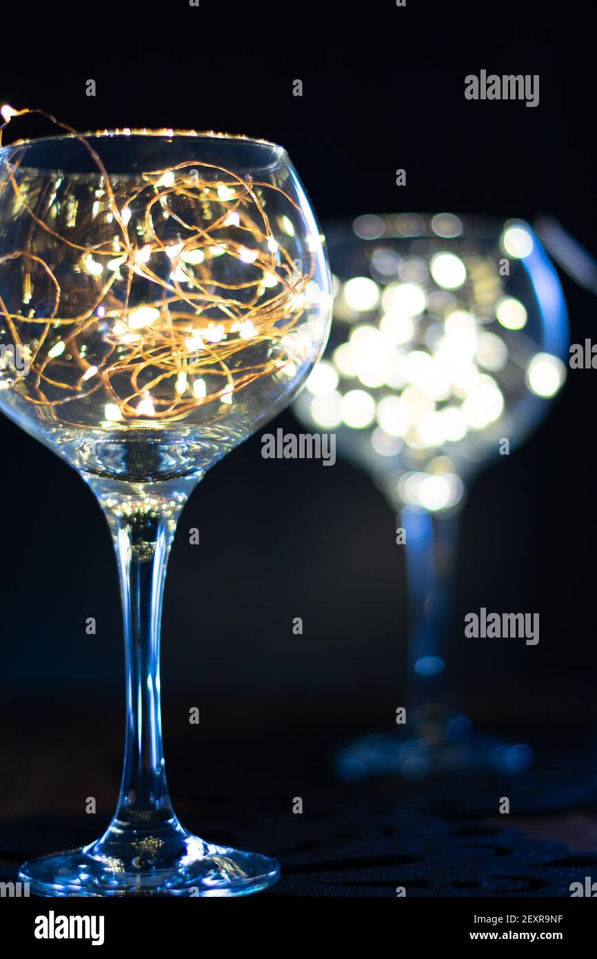 Gin Glas mit Feenlicht im Inneren mit einem anderen im Hintergrund verschwommen, helle Lichter in einem glänzenden Glas vor schwarzem Hintergrund, launisch und stilvoll Stockfoto