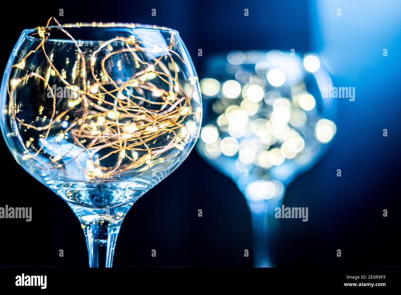 Gin Glas mit Feenlicht im Inneren mit einem anderen im Hintergrund verschwommen, helle Lichter in einem glänzenden Glas vor schwarzem Hintergrund, launisch und stilvoll Stockfoto