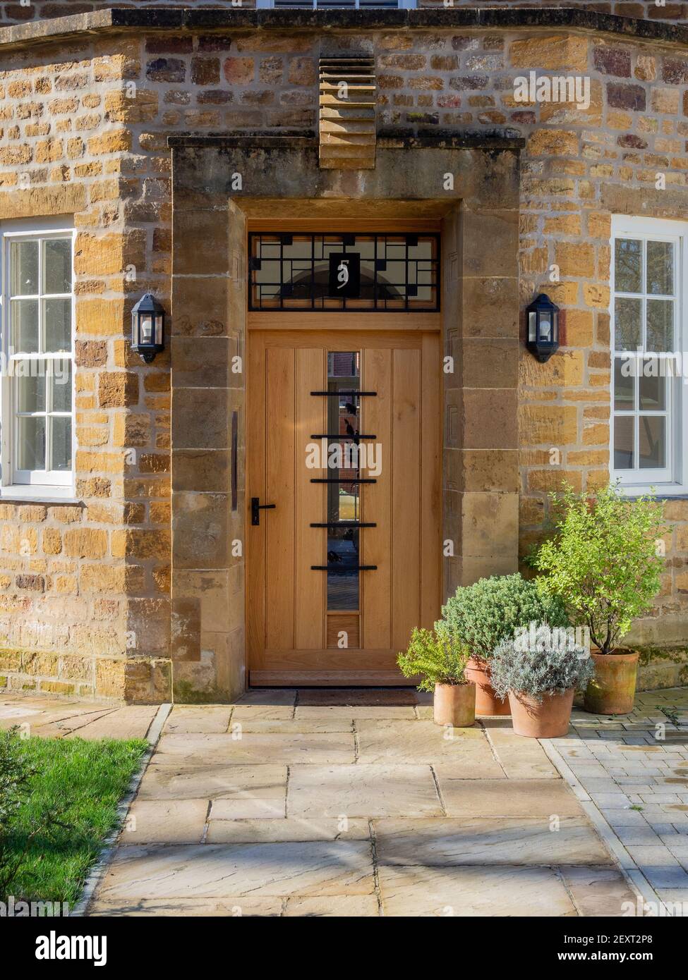 Machen Sie sich auf den Weg zu einer stilvollen, modernen Eingangstür mit einer Sammlung von gepflanzten Terrakotta-Töpfen an einem sonnigen Wintertag, Towcester, Northamptonshire, Großbritannien Stockfoto