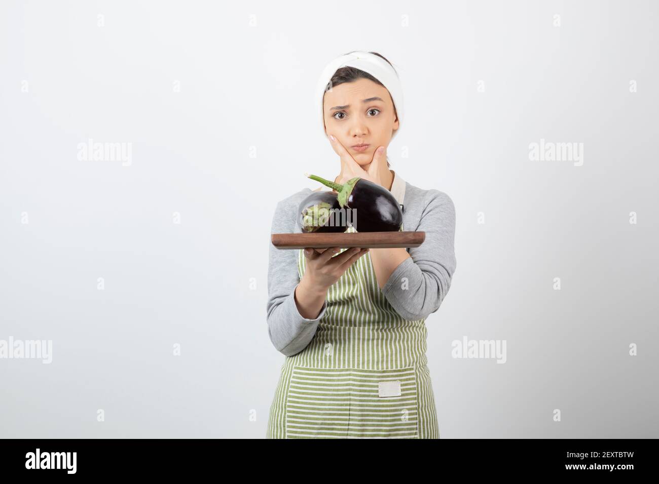 Portrait der weiblichen Köchin hält Platte von großen Auberginen und Denken Stockfoto