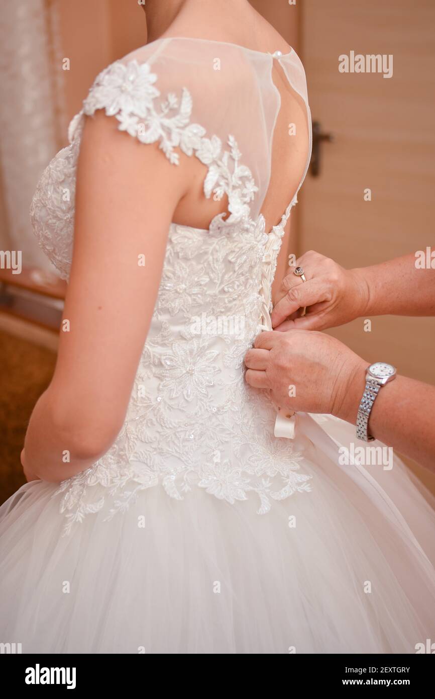 Die Hände einer erwachsenen Frau befestigen das Brautkleid. Stockfoto