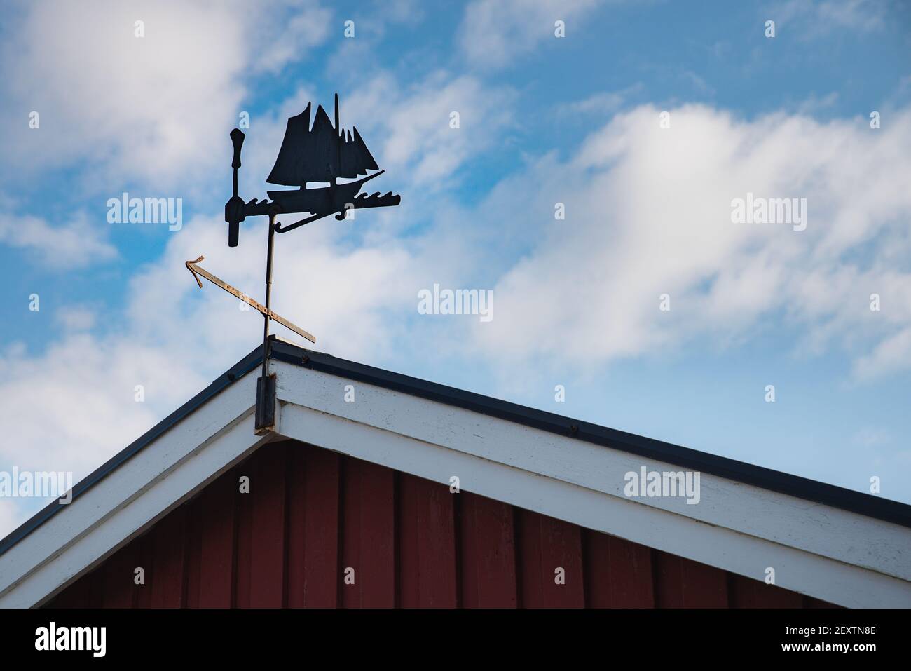 Metallische Wetterfahne auf einem schrägen Dach ähnelt einem alten Wikinger-Segelschiff oder einer Galeere, die die Windrichtung anzeigt. Alte Segelboot Windfahne Stockfoto