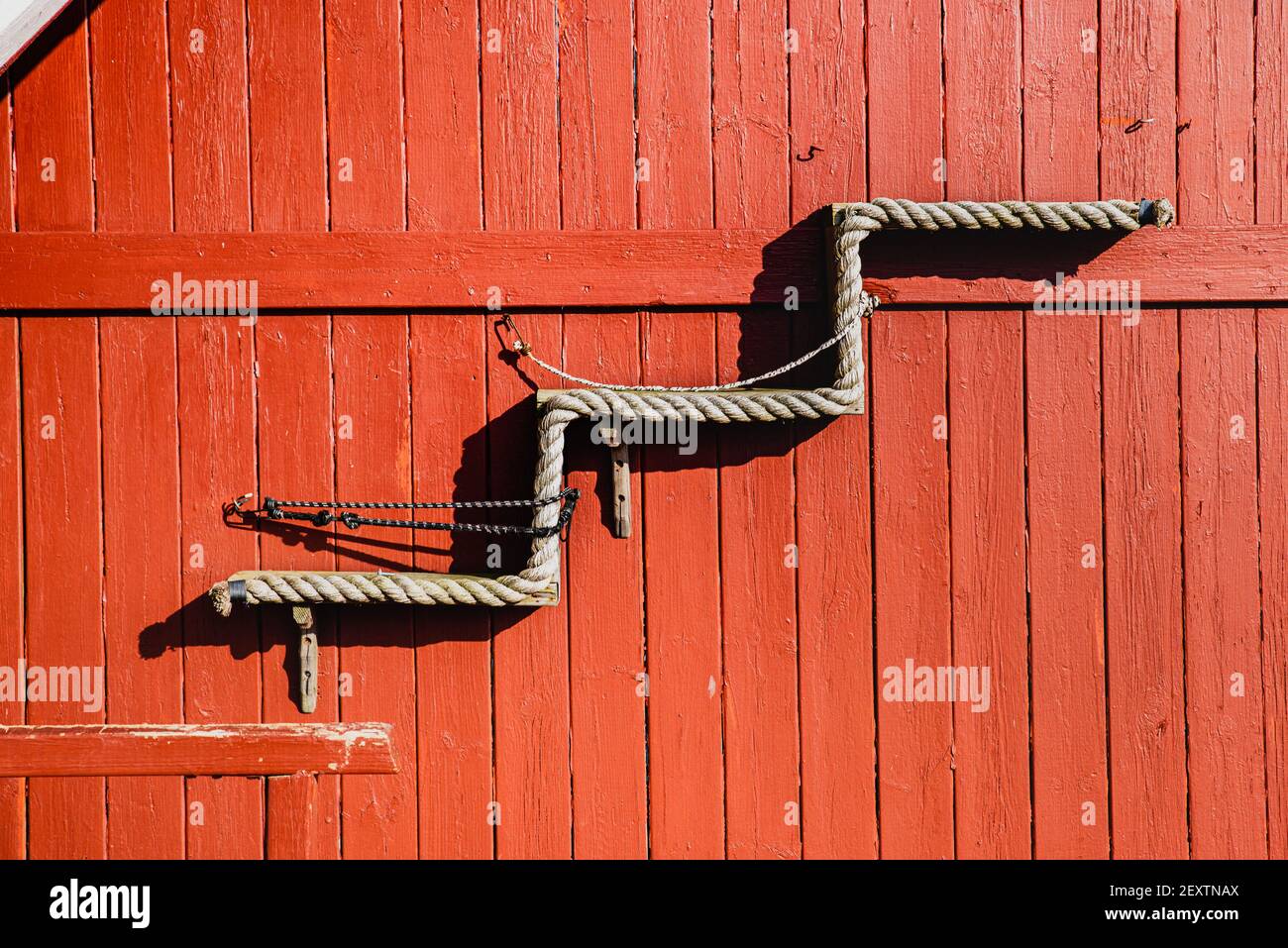 Treppe steigt nach oben aus einem Seil auf rotem Holzhintergrund aus Holzplanken Muster erstellt. Das Detail der Fassade des roten Hauses stellt die aufrassenden Stufen dar Stockfoto