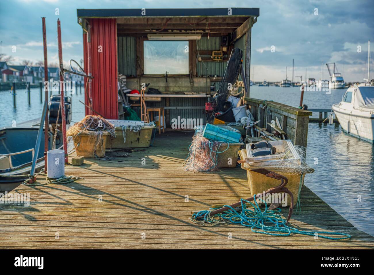 Ein rostiger Anker mit einem hellblauen Seil, das an einem hölzernen Pier befestigt ist. Fischerhütte mit vielen Angelgeräten in einem Fischerdorf oder Fischerhafen Stockfoto