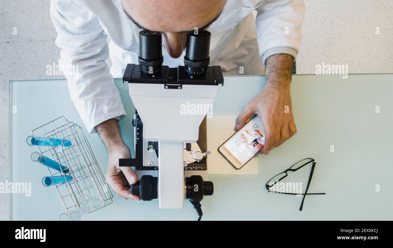 Reifer Wissenschaftler männlich in seinem 50s trägt einen Laborkittel Blick durch ein Mikroskop in einem Labor. Baskenland, Spanien, Europa. Stockfoto