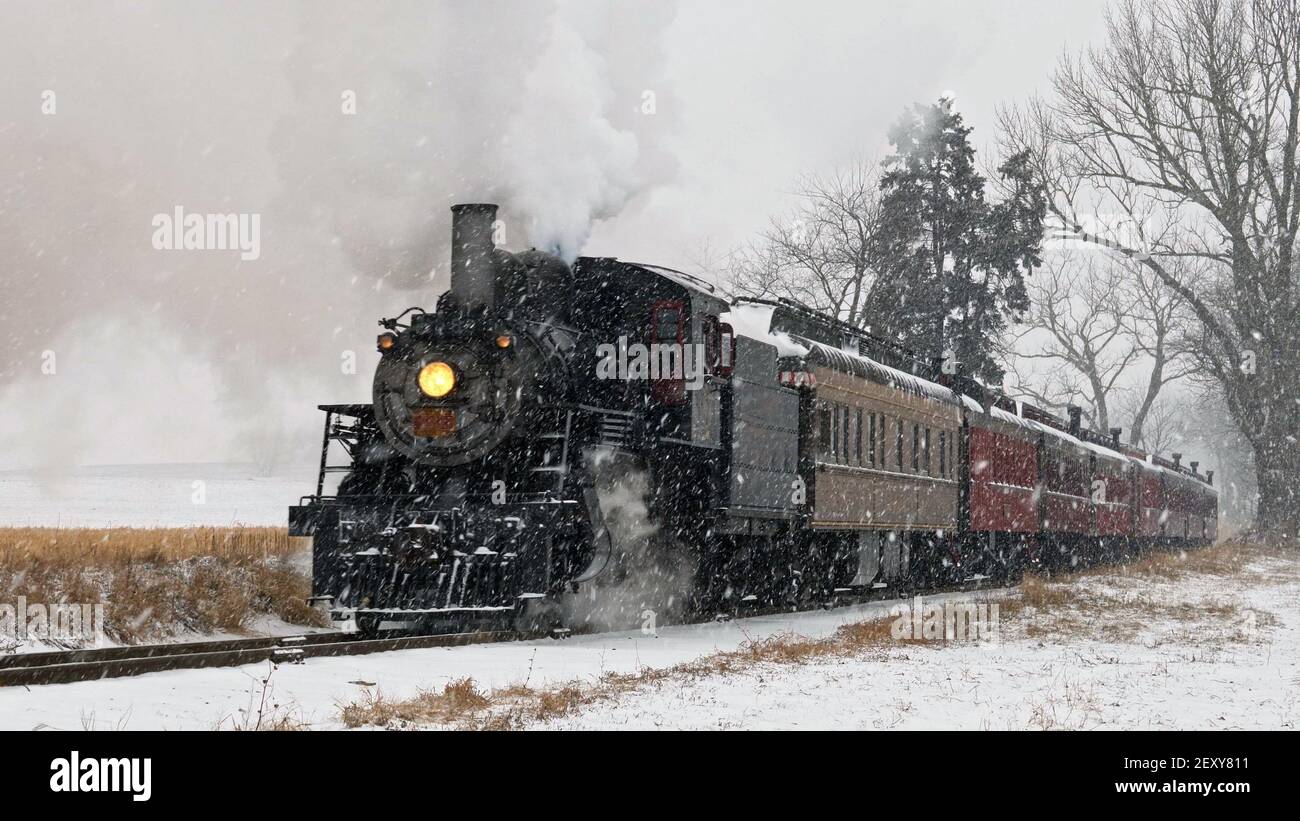 Blick auf eine antike restaurierte Dampflokomotive weht Rauch und Dampf Reisen durch Ackerland und Landschaft in einem Schneesturm Stockfoto