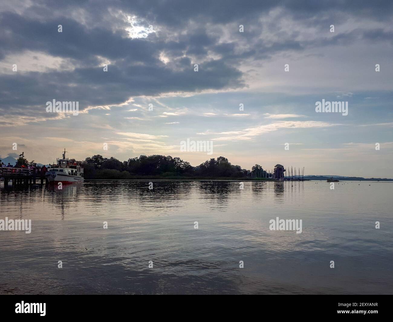 Sonnenuntergang über dem Chiemsee mit Baumsilhouetten am Horizont im Sommer. Ruhige Szene mit Wasser und wolkendem Abendhimmel Stockfoto