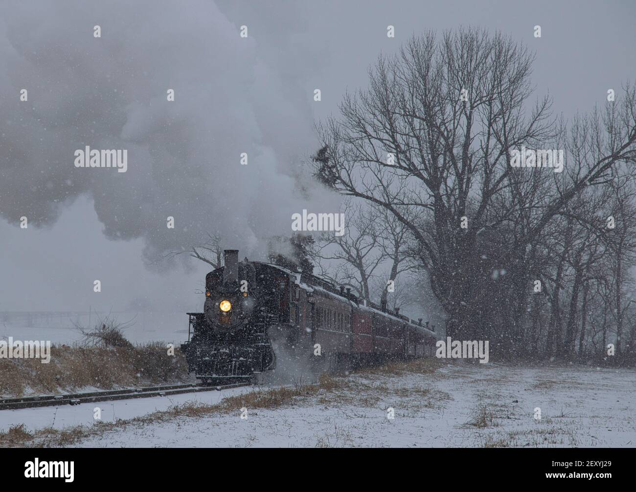Blick auf eine antike restaurierte Dampflokomotive weht Rauch und Dampf Reisen durch Ackerland und Landschaft in einem Schneesturm Stockfoto
