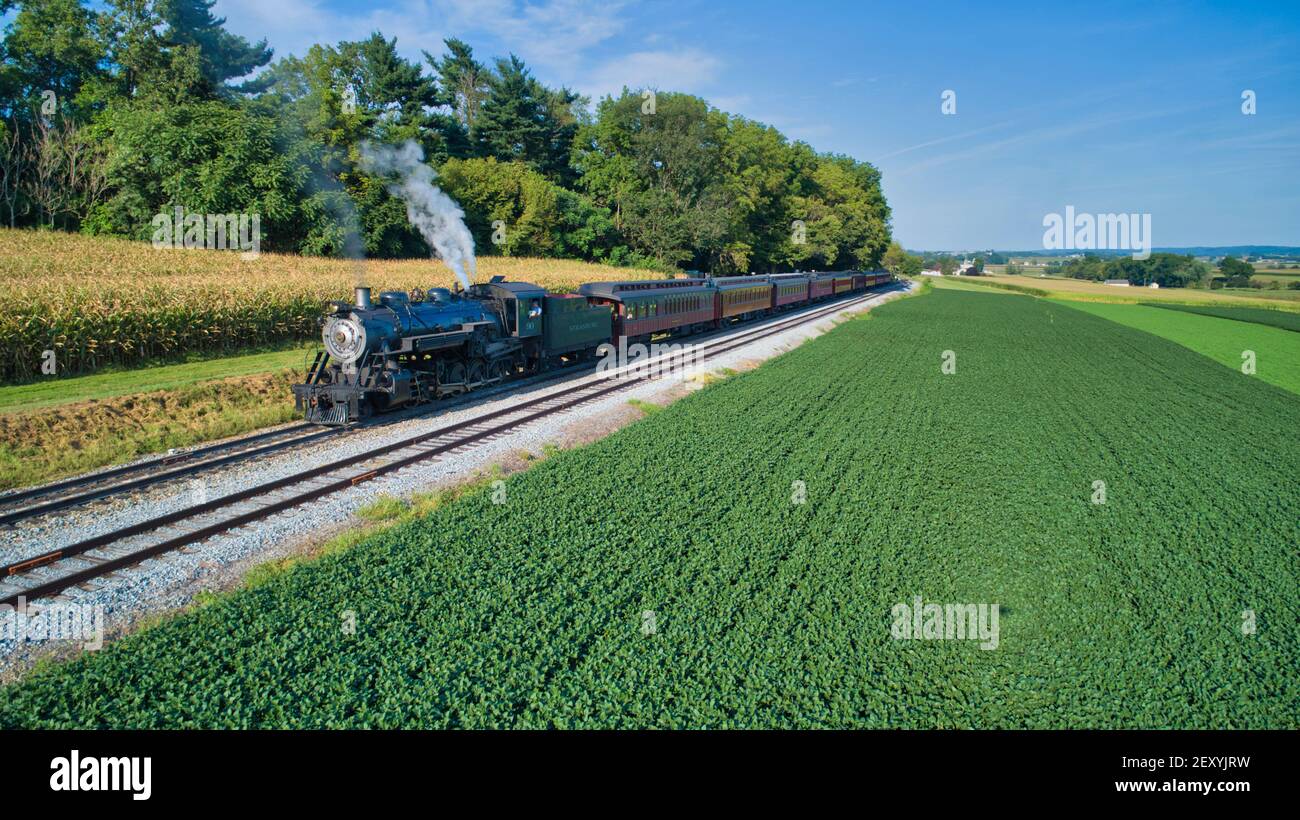 Luftaufnahme einer antiken restaurierten Dampflokomotive, die Rauch bläst Und Dampf Reisen durch Ackerland und Landschaft auf einem sonnigen Sommertag Stockfoto