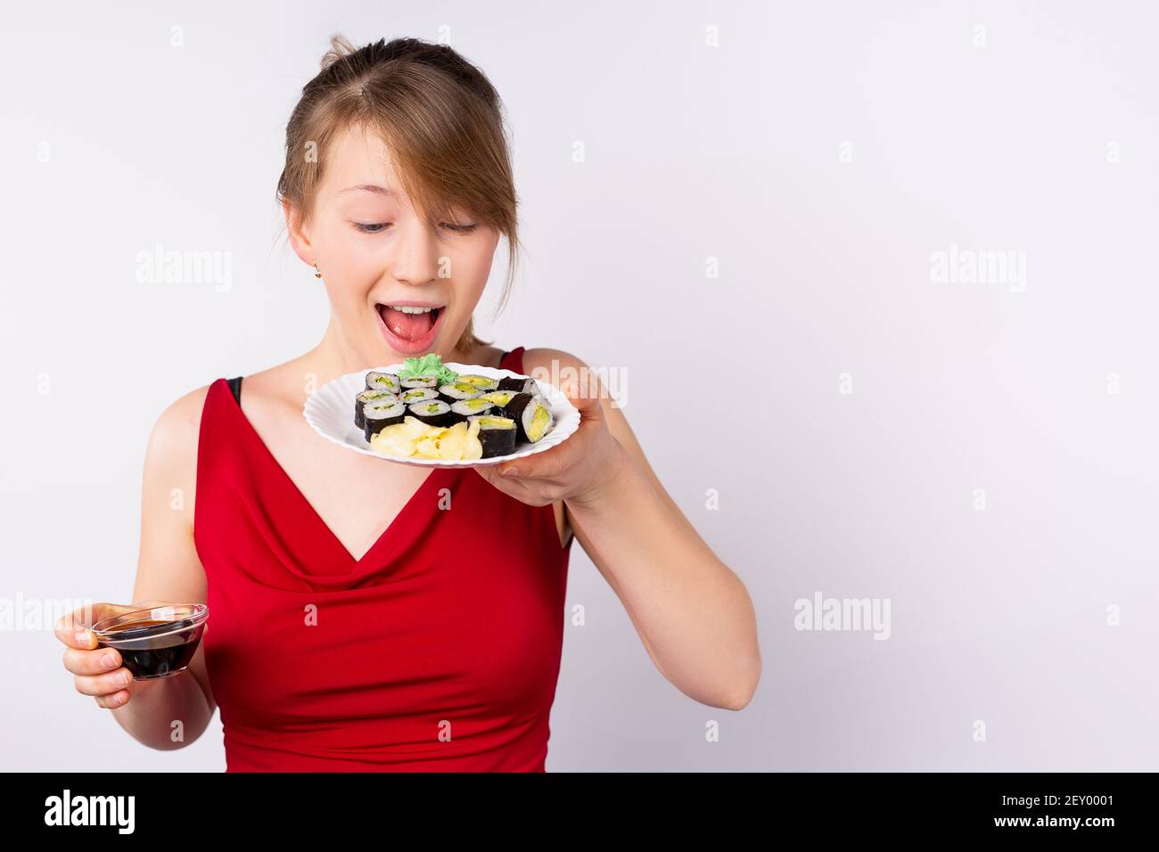 Ein stilvolles junges lächelndes Mädchen posiert, hält einen Teller mit Brötchen und Sojasauce in der anderen Hand. Appetitlich Werbefotografie für Restaurant, Sushi Stockfoto