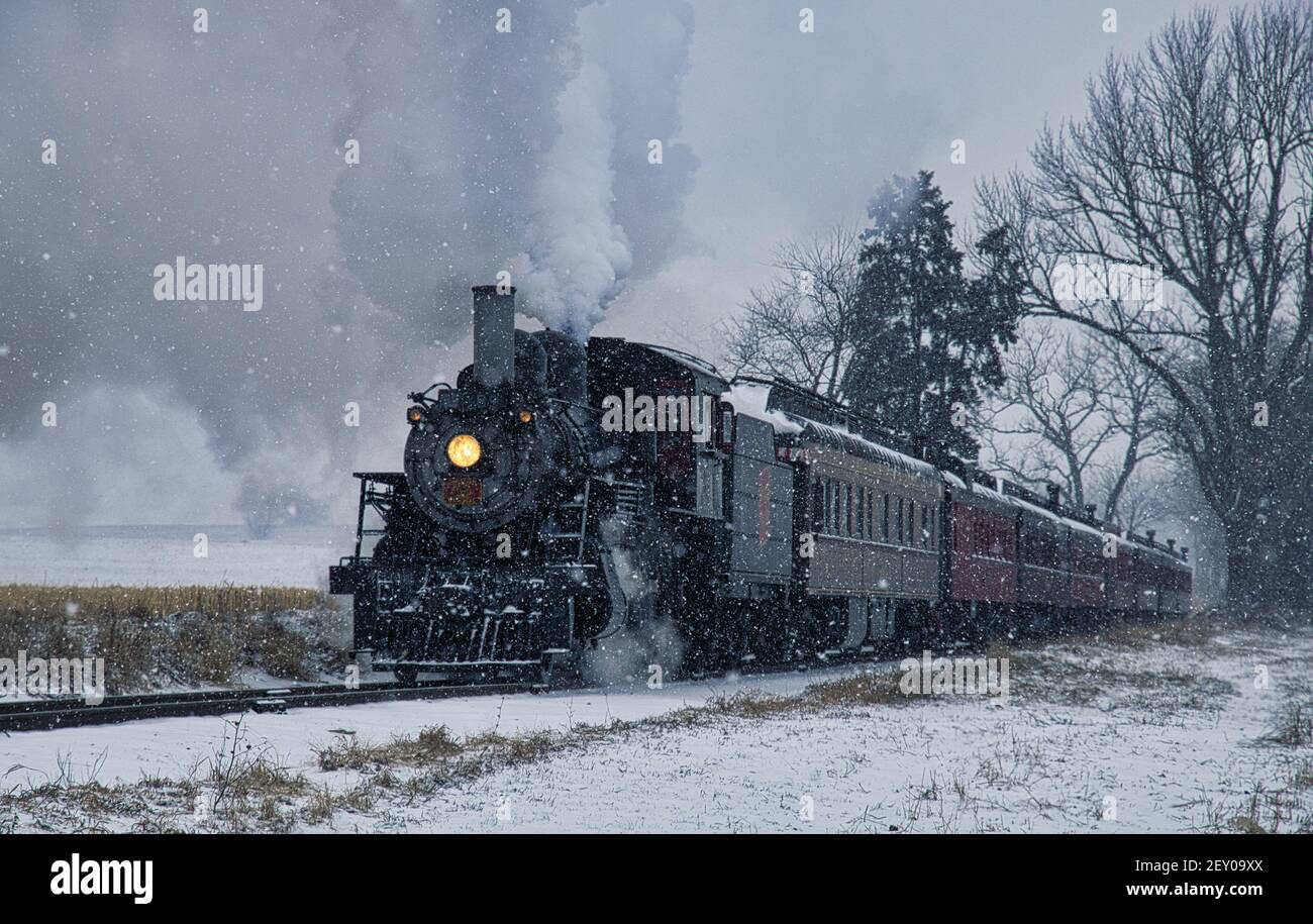 Blick auf eine antike restaurierte Dampflokomotive weht Rauch und Dampf Reisen durch Ackerland und Landschaft in einem Schneesturm Stockfoto