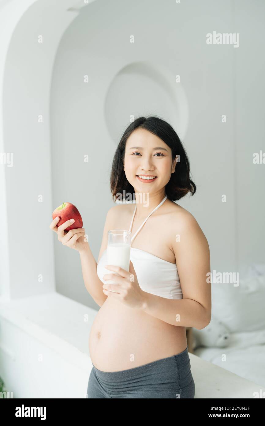 Schwangere Frau mit hübschen Magen hält roten Apfel und eine Flasche Milch, schwangere Mutter schaut nach unten Stockfoto