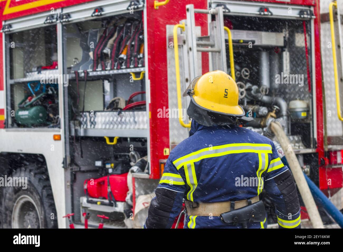 Ausrüstung und Feuerwehrmann von Feuerwehrwagen. Feuerwehrmann in Helm und Uniform geht mit Werkzeugen in einen Feuerwehrwagen Stockfoto