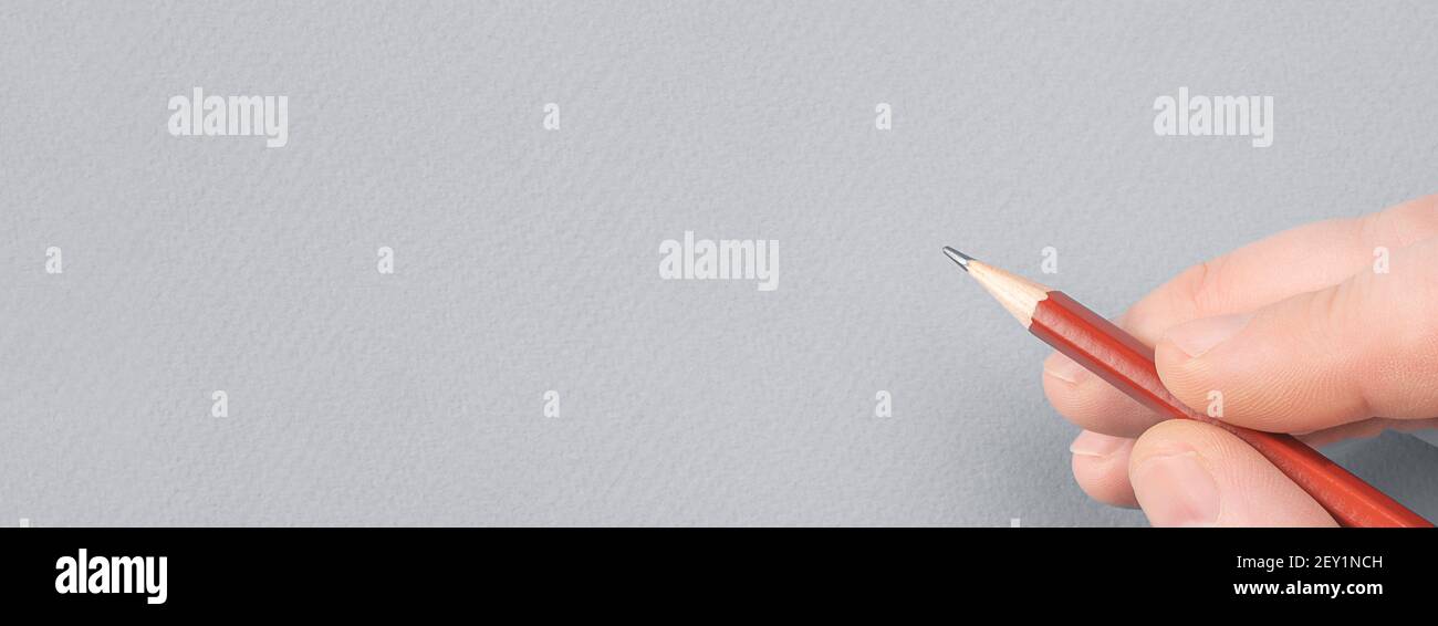 Ein Mann die Hand mit dem Bleistift auf grauem Papier Hintergrund. Copy Space. Nahaufnahme Der Menschlichen Hand Mit Bleistift. Menschliche Hand Zeichnung mit Bleistift auf leerem Grau Stockfoto