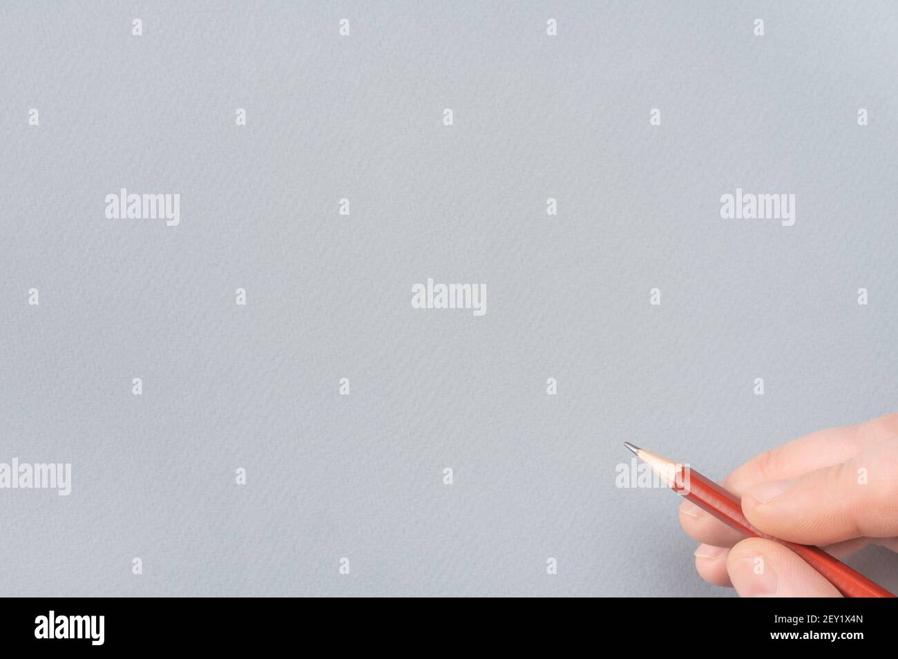 Ein Mann die Hand mit dem Bleistift auf grauem Papier Hintergrund. Copy Space. Nahaufnahme Der Menschlichen Hand Mit Bleistift. Menschliche Hand Zeichnung mit Bleistift auf leerem Grau Stockfoto