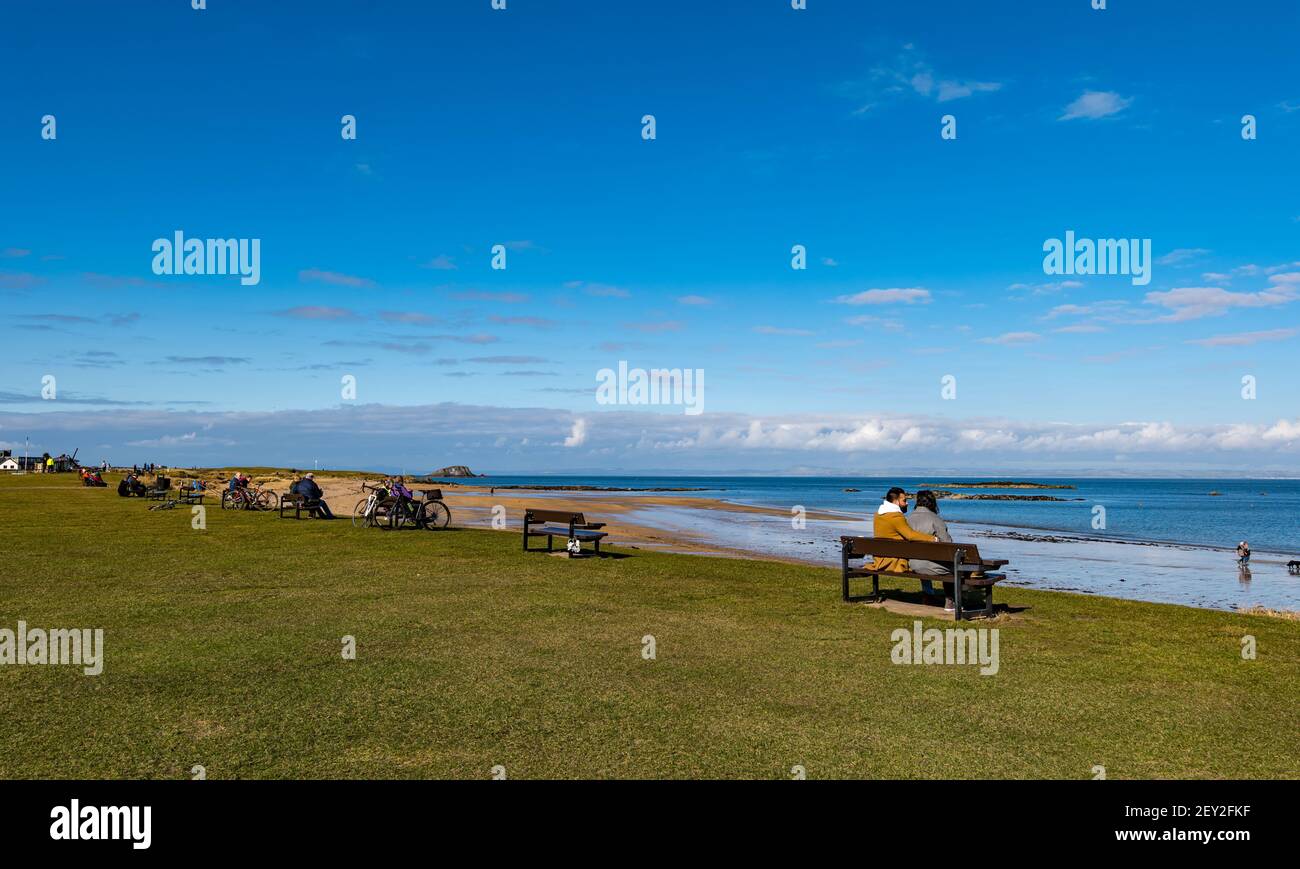 Menschen sitzen auf Bänken am Strand mit Blick auf Firth of Forth, North Berwick, East Lothian, Schottland, Großbritannien Stockfoto