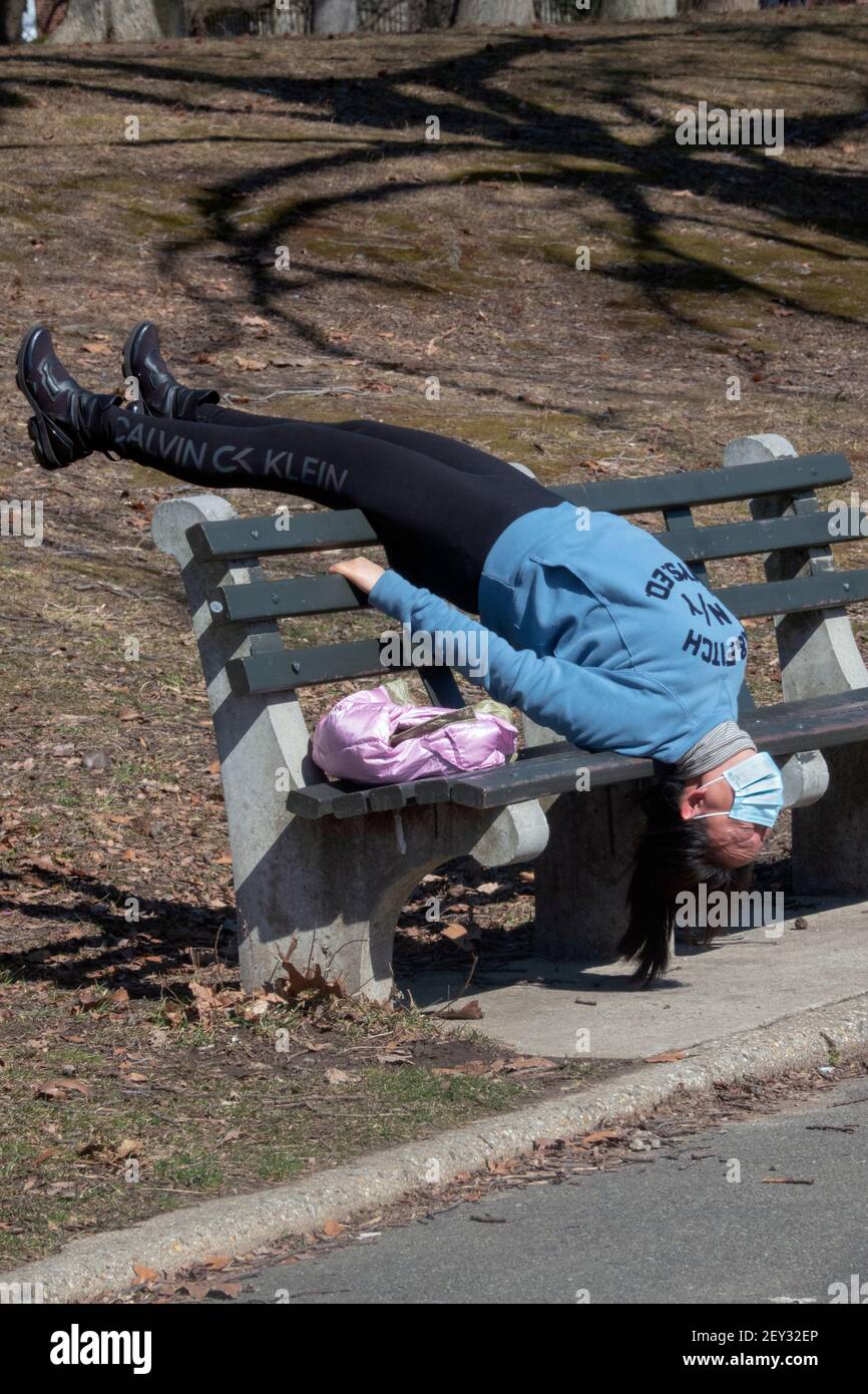 Eine asiatisch-amerikanische Frau, wahrscheinlich Chinesin, macht eine sehr ungewöhnliche Strecke auf dem Kopf auf einer Bank in einem Park in Queens, New York City Stockfoto