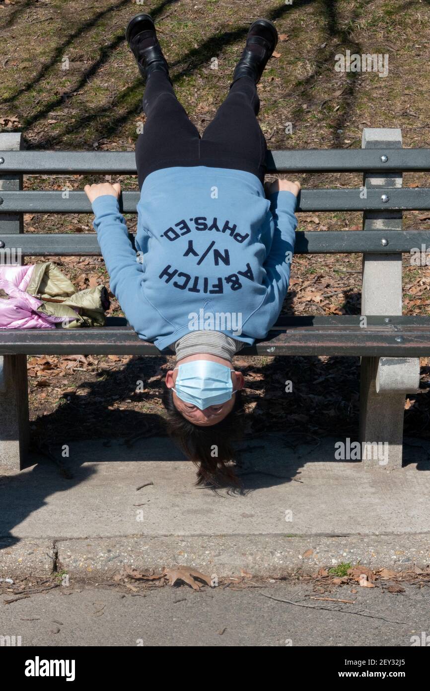 Eine asiatisch-amerikanische Frau, wahrscheinlich Chinesin, macht eine sehr ungewöhnliche Strecke auf dem Kopf auf einer Bank in einem Park in Queens, New York City Stockfoto