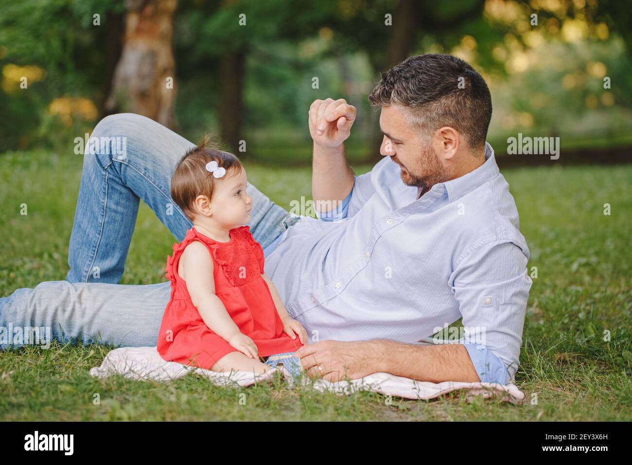 Mittelalter kaukasischen stolzen Vater spielt mit Baby Tochter. Familie Vater und Tochter sitzen zusammen im Freien im Park am Sommertag. Das Leben mit Kindern Stockfoto